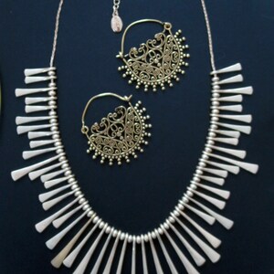 May include: A silver necklace with a fringe design and a pair of gold filigree hoop earrings. The necklace is made of small silver beads and has a delicate, feminine look.