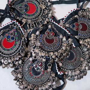 May include: A set of five silver-toned jewelry pieces with red, blue, and green glass stones. Each piece features a crescent moon shape with a mirror in the center. The pieces are attached to black fabric with white beads.