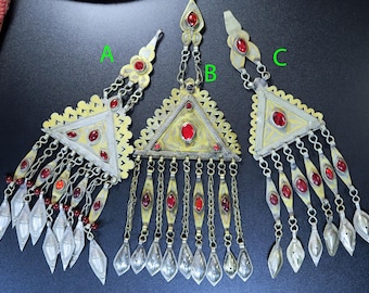 May include: Three ornate, silver-toned pendants with red gemstone accents. Each pendant features a triangular design with intricate detailing and dangling chains ending in teardrop shapes. The pendants are likely jewelry.