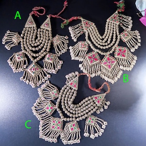May include: Three ornate silver necklaces with matching earrings. Each necklace features multiple strands of small beads, triangular pendants, and square pendants with red and green accents. The earrings have a similar design, with dangling elements.