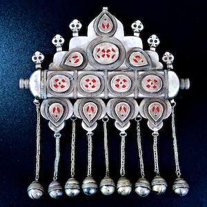 May include: A silver pendant with red accents and a decorative design. The pendant has a central section with a series of small, round, red accents and a series of dangling bells.