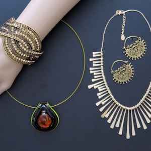 May include: A set of gold-tone jewelry featuring a necklace with a fringe design, a pair of earrings with a circular filigree design, and a bracelet with a multi-layered design with rhinestones.