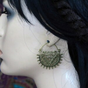 May include: A pair of gold-toned hoop earrings with a detailed, intricate design. The earrings are in the shape of a crescent moon with a floral pattern.