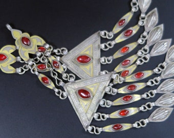 May include: A pair of silver and gold triangular pendants with red gemstone accents. The pendants are connected by a chain and have intricate designs.