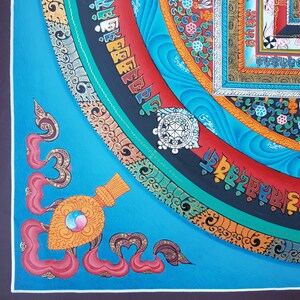 May include: A colourful Tibetan mandala painting with intricate details and a blue background. The mandala features a central circle with a wheel-like design, surrounded by concentric circles of geometric patterns and text in Tibetan script.