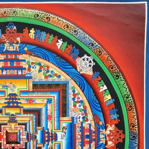May include: A colorful mandala painting with intricate details and a red, green, and blue border. The mandala features a central square with a series of concentric circles and geometric patterns. The painting is framed in a dark wood frame.