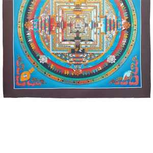 May include: A colourful mandala with a blue background and intricate details. The mandala is surrounded by a border of gold and red. The centre of the mandala is a square with a smaller square inside. The mandala is a traditional Tibetan Buddhist symbol of the universe.
