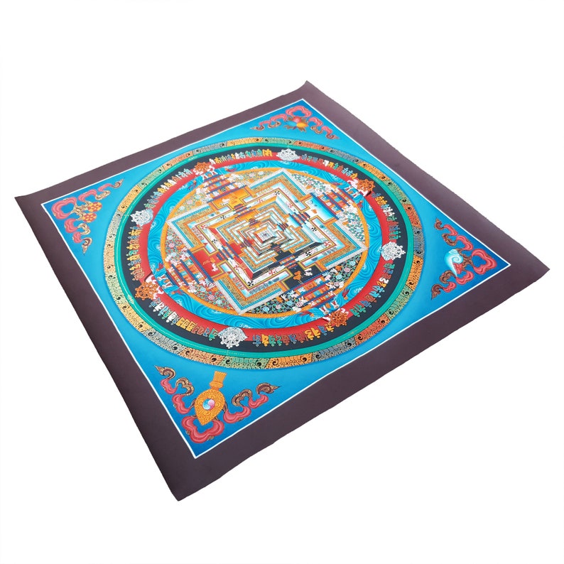 May include: A colourful mandala print on a dark brown background. The mandala features a square with concentric circles and intricate details in shades of blue, red, yellow, and green. The print is surrounded by a decorative border.