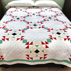 May include: A white quilt with a geometric pattern in red, green, and black. The quilt is made of cotton and has a traditional design.