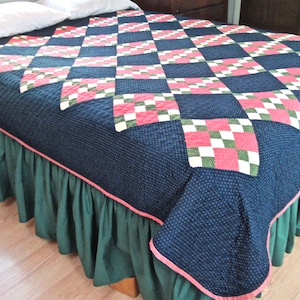 May include: A navy blue quilt with a pink and green checkered pattern. The quilt is on a bed with a green bed skirt.