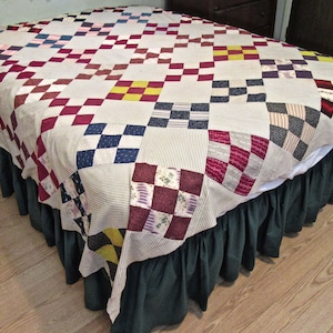 May include: A patchwork quilt with a variety of colors and patterns, including red, blue, yellow, and white. The quilt is laid out on a bed with a green bed skirt.