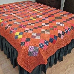May include: A patchwork quilt with a variety of colors and patterns, including red, pink, blue, yellow, and green. The quilt is made of squares and is laid out on a bed with a dark green bed skirt.