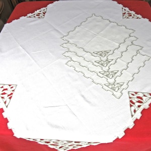 May include: A set of four white linen placemats with delicate embroidered lace trim. The placemats are stacked on top of each other, and the lace trim is visible on all four sides.