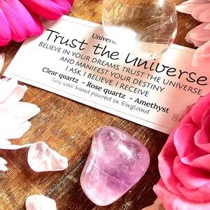 May include: A set of three crystals, clear quartz, rose quartz, and amethyst, with a card that reads "Trust the Universe. Believe in your dreams, trust the universe and manifest your destiny. I ask, I believe, I receive. Clear quartz - Rose quartz - Amethyst. Soy wax hand poured in England."