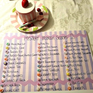 May include: A decorative arrangement featuring a pink and white striped container with a red cherry, a plate, and a list of "Mystery Bookish Scoops" with book-themed accessories and stationery items.