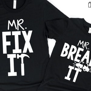 May include: Two black t-shirts with white text. The larger shirt says "Mr. Fix It" with a hammer and nail graphic. The smaller shirt says "Mr. Break It" with a car graphic.