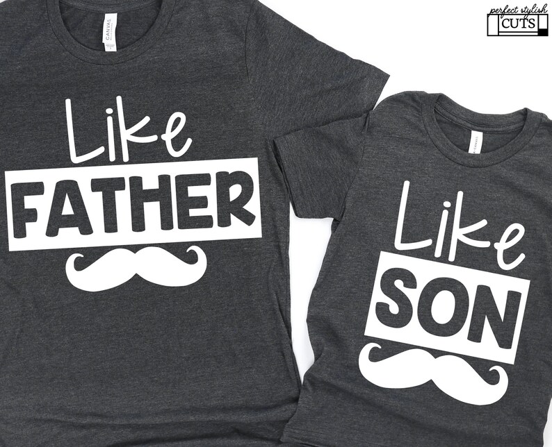 May include: Two gray t-shirts with white text and a white mustache graphic. The larger shirt says "Like Father" and the smaller shirt says "Like Son".