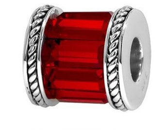 Puede incluir: Una cuenta roja rectangular con un diseño facetado. La cuenta está encerrada en un engaste de metal plateado con un diseño de cuerda trenzada en los bordes. La cuenta tiene un agujero en el centro.