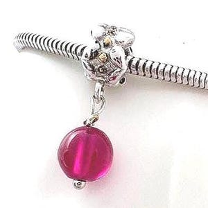 May include: A silver charm bracelet with a floral design and a dangling magenta bead. The charm features gold accents and a textured silver band, showcasing a blend of elegance and detail.