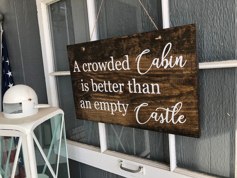 May include: A wooden sign with white text that reads "A crowded Cabin is better than an empty Castle".