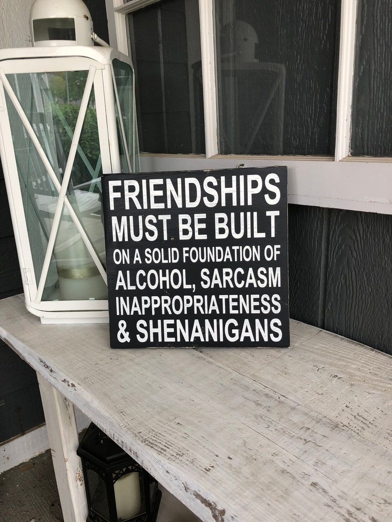 May include: Black wooden sign with white text that reads "Friendships must be built on a solid foundation of alcohol, sarcasm, inappropriateness & shenanigans."