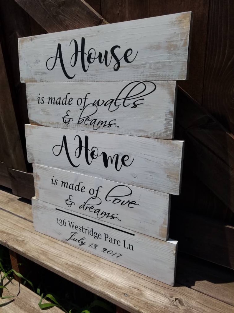 May include: A white wooden sign with black lettering that reads "A House is made of walls & beams. A Home is made of love & dreams." The sign also includes the address "136 Westridge Parc Ln" and the date "July 13, 2017".