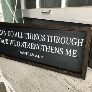 Op de afbeelding: Een zwart houten bord met witte tekst die luidt: "Ik kan alles doen door Hem die mij kracht geeft Dani&euml;l 24:7".