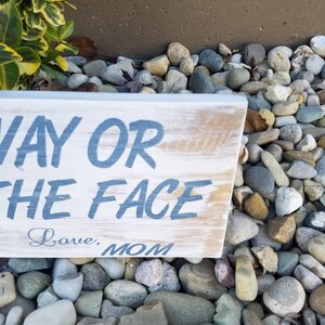 Pu&ograve; includere: Un cartello in legno rustico con il testo "Way or the Face" in vernice blu. Il cartello &egrave; invecchiato e ha un aspetto vissuto. Sotto il testo, &egrave; scritto "Love, Mom" in corsivo.