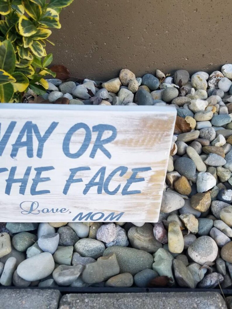 Pu&ograve; includere: Un cartello in legno rustico con il testo "Way or the Face" in vernice blu. Il cartello &egrave; invecchiato e ha un aspetto vissuto. Sotto il testo, &egrave; scritto "Love, Mom" in corsivo.