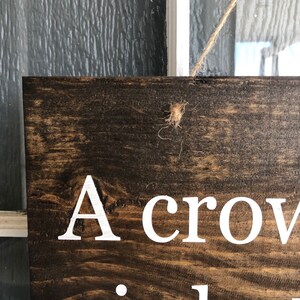 May include: A wooden sign with the text "A crow..." in white paint. The sign is hanging from a string.