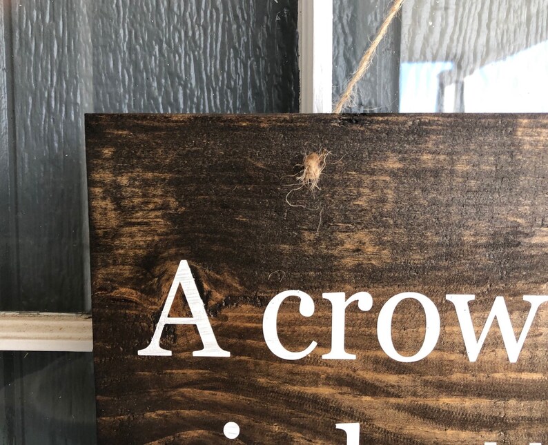 May include: A wooden sign with the text "A crow..." in white paint. The sign is hanging from a string.