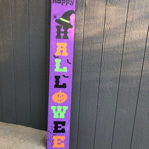 May include: Purple wooden sign with the words "Happy Halloween" in black, orange, and green letters. The sign has a witch's hat, bats, a spider, and a pumpkin on it.