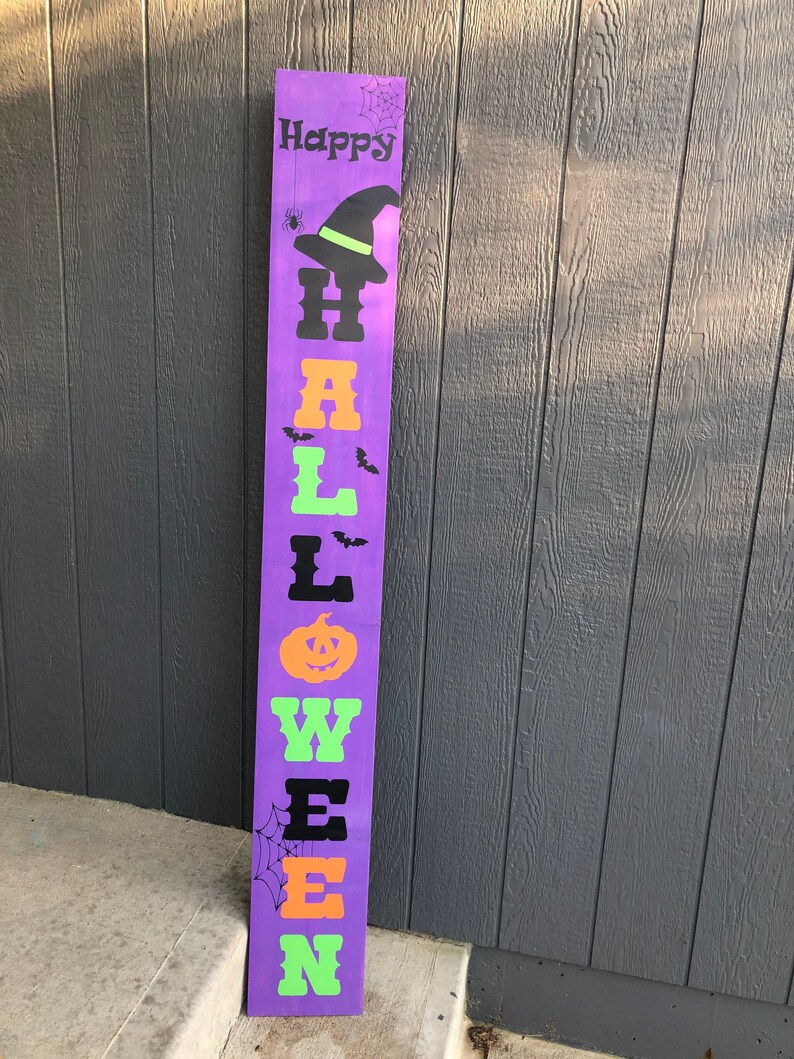 May include: Purple wooden sign with the words "Happy Halloween" in black, orange, and green letters. The sign has a witch's hat, bats, a spider, and a pumpkin on it.