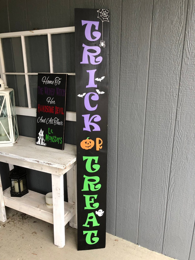 May include: Black wooden sign with the words "Trick or Treat" in green and purple letters. The sign has a spider web, spider, bats, a pumpkin, and a ghost.
