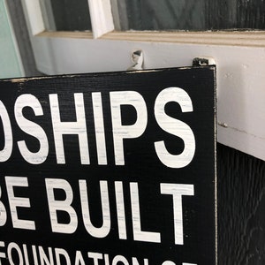 May include: Black wooden sign with white text that reads "Friendships are built on a foundation of mutual sarcasm".