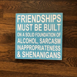 May include: A blue wooden sign with white text that reads "Friendships must be built on a solid foundation of alcohol, sarcasm, inappropriateness & shenanigans."