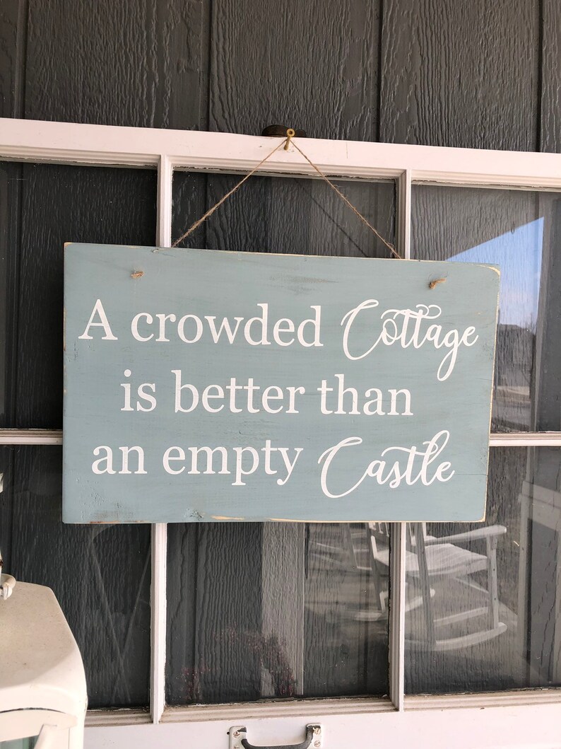 May include: A blue wooden sign with white lettering that reads "A crowded Cottage is better than an empty Castle".
