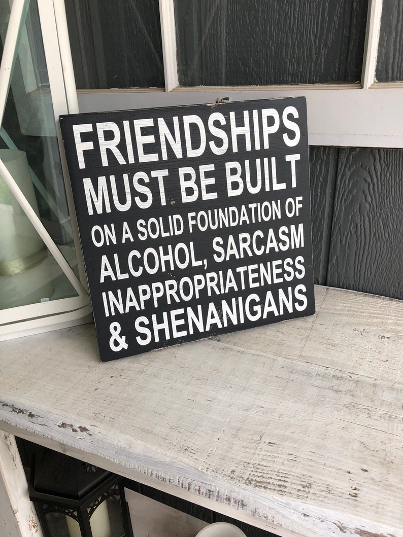May include: Black wooden sign with white text that reads "Friendships must be built on a solid foundation of alcohol, sarcasm, inappropriateness & shenanigans."