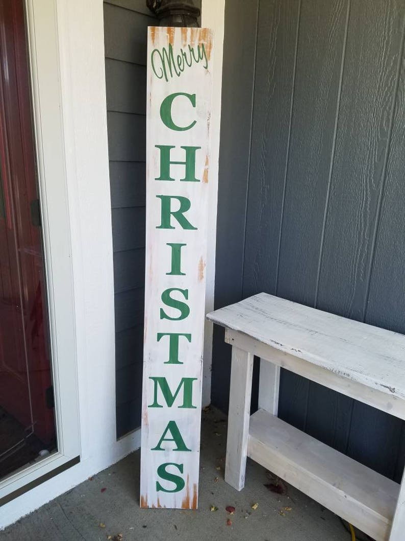 Puede incluir: Un letrero de madera blanco con las palabras "Merry Christmas" en letras verdes. El letrero est&aacute; apoyado en una mesa de madera blanca.