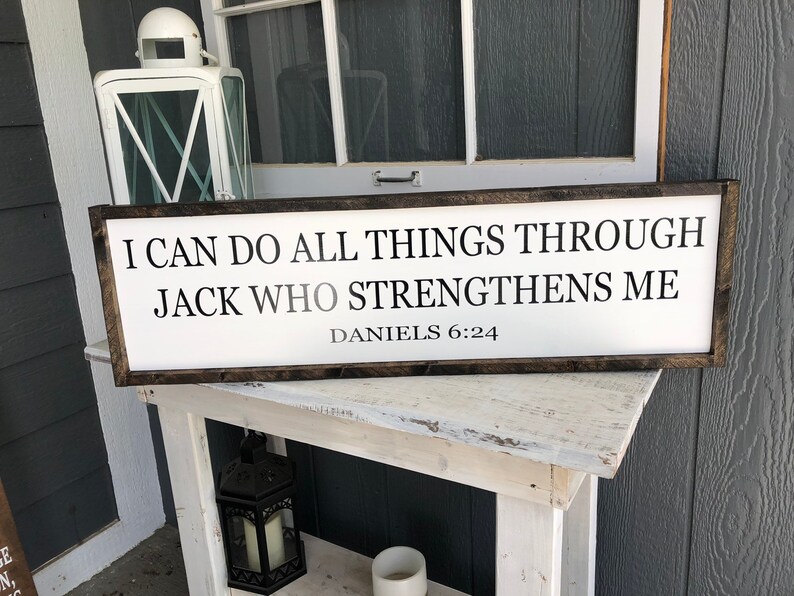 Op de afbeelding: Een wit houten bord met zwarte tekst die luidt: "Ik kan alles door Jack doen die mij sterkt Dani&euml;l 6:24".