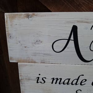 May include: A white wooden sign with black lettering that reads "A home is made with love & laughter".