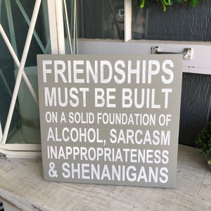 May include: A grey wooden sign with white text that reads "Friendships must be built on a solid foundation of alcohol, sarcasm, inappropriateness & shenanigans."