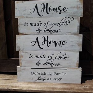 May include: A white wooden sign with black lettering that reads "A House is made of walls & beams. A Home is made of love & dreams." The sign also includes the address "136 Westridge Parc Ln" and the date "July 13, 2017".