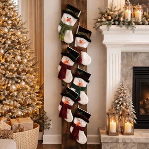May include: A wooden board with six snowman-themed Christmas stockings. Each stocking has a black top hat, an orange carrot nose, and a scarf in various colors. The text "And the Stockings were hung..." is above the stockings.