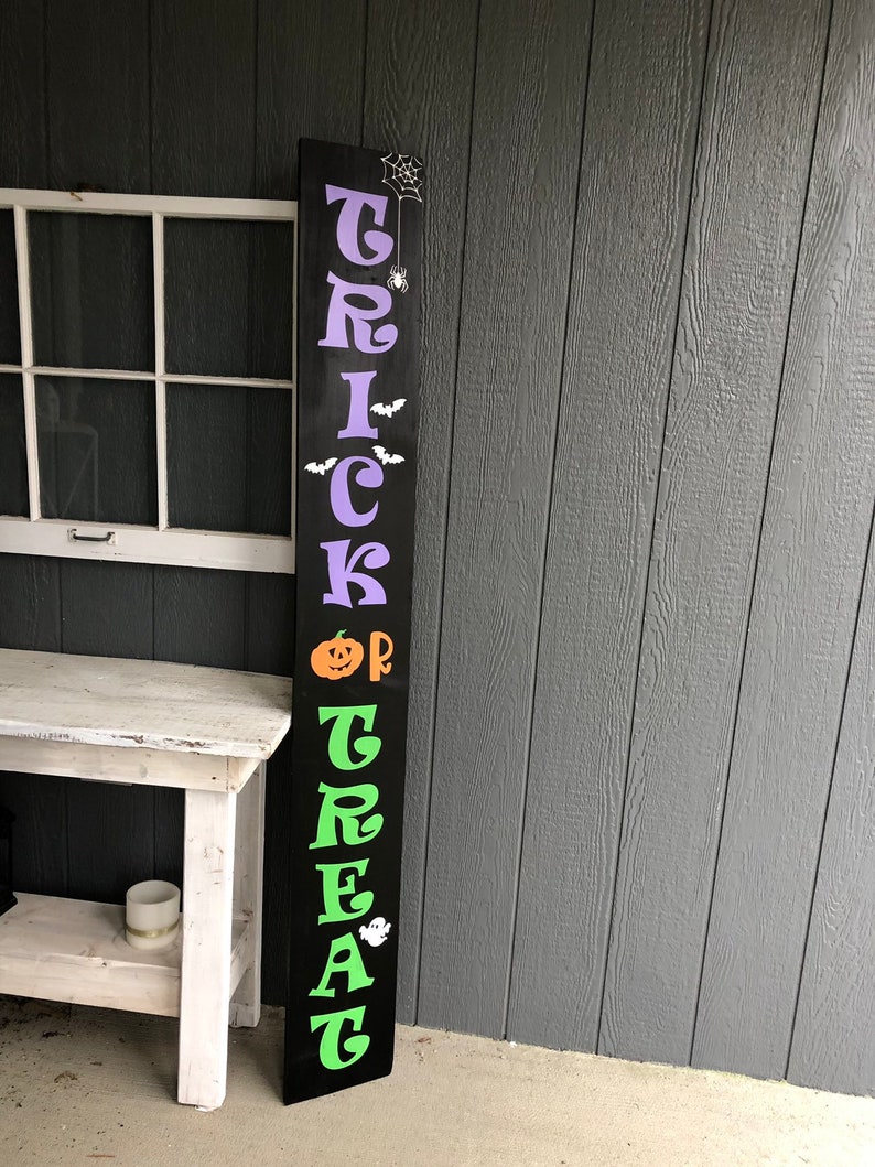 May include: Black wooden sign with the words "Trick or Treat" in purple, green, and orange letters. The sign has a spider web and spider, bats, a pumpkin, and a ghost.