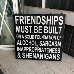 May include: Black wooden sign with white text that reads "Friendships must be built on a solid foundation of alcohol, sarcasm, inappropriateness & shenanigans."