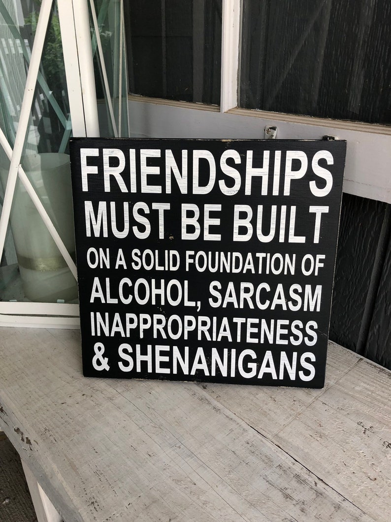 May include: Black wooden sign with white text that reads "Friendships must be built on a solid foundation of alcohol, sarcasm, inappropriateness & shenanigans."