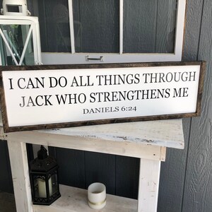 Op de afbeelding: Een wit houten bord met zwarte tekst die luidt: "Ik kan alles door Jack doen die mij sterkt" en "Daniels 6:24".