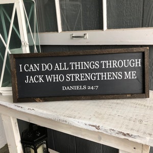 Op de afbeelding: Een donkerbruin houten bord met witte tekst die luidt: "Ik kan alles door Hem die mij kracht geeft. Dani&euml;l 24:7".