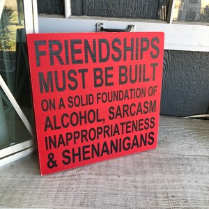 May include: Red wooden sign with black text that reads "Friendships must be built on a solid foundation of alcohol, sarcasm, inappropriateness & shenanigans."